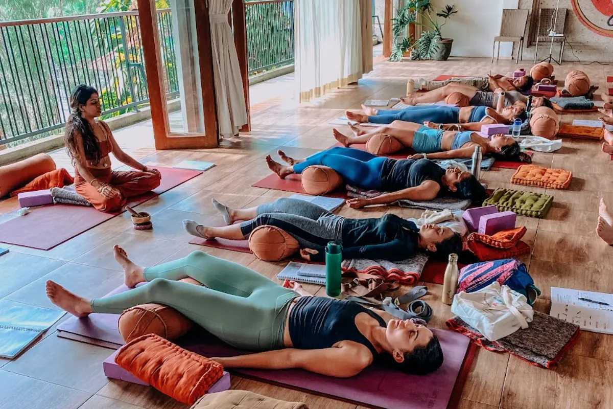YNV - Students in Savasana with Instructor Seated Watching Over Class